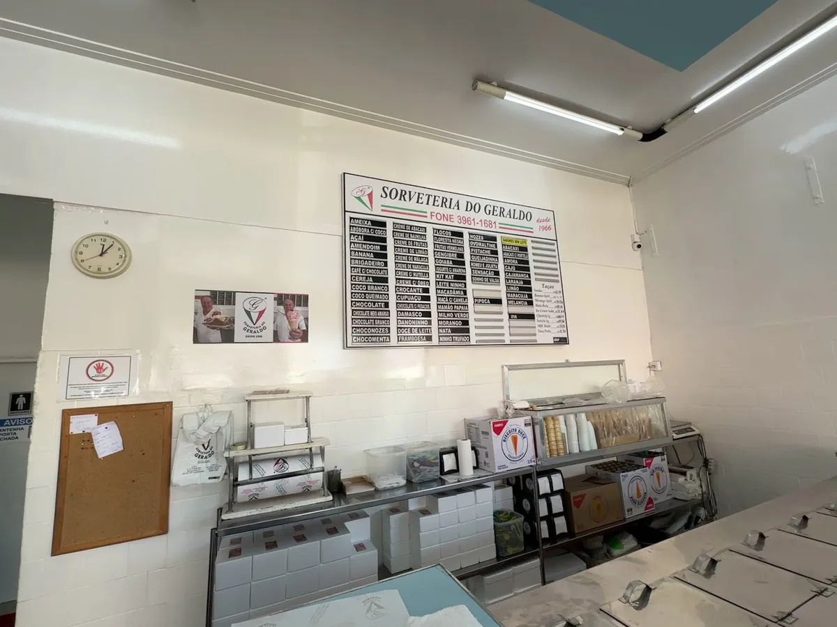 Balcão da sorveteria com azulejo branco, freezers e o quadro de sabores na parede